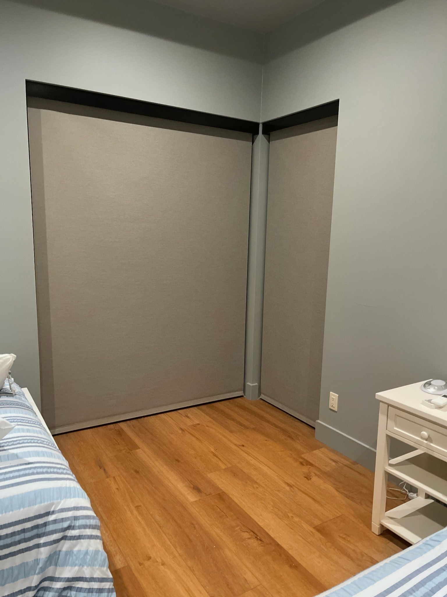 Floor-length roller shades covering corner bedroom windows
