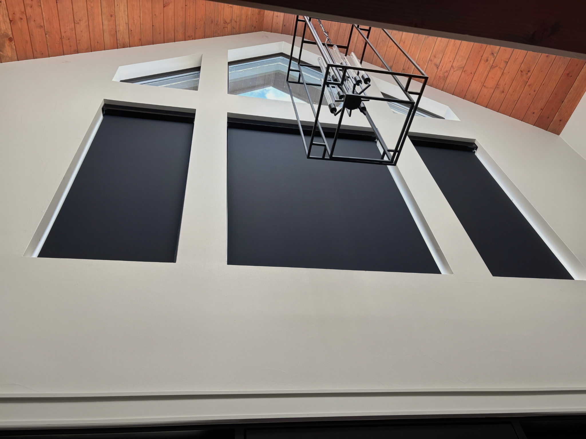 Black shades fitted to high windows beneath a vaulted wood ceiling