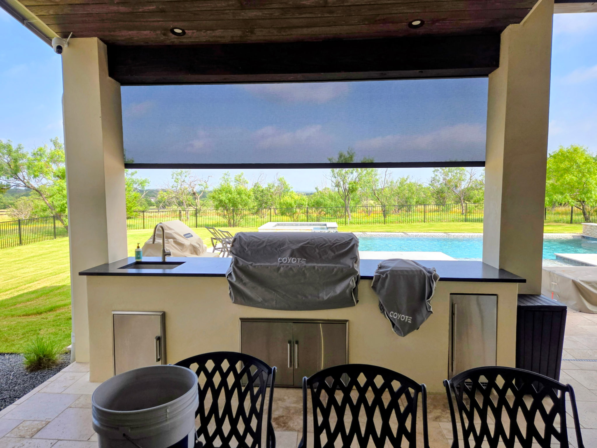 Outdoor roller shade above a poolside kitchen